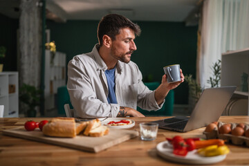 Young man enjoying coffee and smiling during breakfast remote work