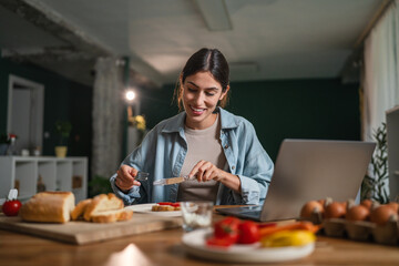 Woman eating healthy breakfast using laptop at home