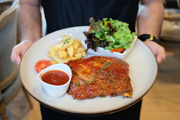 Delicious BBQ ribs with sides, served on a plate and held by a person. The ribs are coated in a...