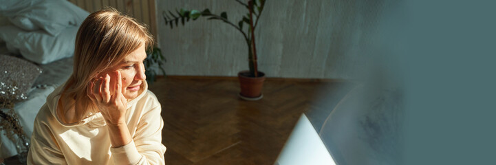 Thoughtful caucasian mature female in cozy room with indoor plant and soft natural lighting.