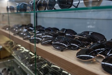 A close-up view of various sunglasses displayed on a wooden shelf in a retail store. The glasses...