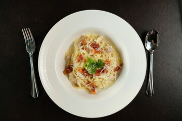 A delicious plate of creamy spaghetti carbonara, ready to be enjoyed. Beside are silver utensils: a fork and a spoon.