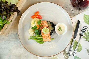 A top-down view of a gourmet salmon dish, artfully presented on a plate. It features grilled salmon, mashed potato, greens, and a sauce.