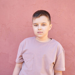Caucasian young male child in pink t-shirt standing against textured wall.