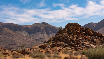 A rocky outcrop against a mountain range and great cloudscape in the Richtersveld in the Northern Cape of South Africa