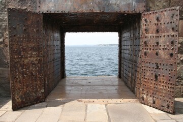 Large, rusty, open metal gates reveal a view of the ocean and horizon