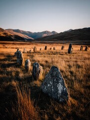 Ancient standing stones circle in a golden field, backlit by a mountain landscape