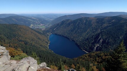 High angle panorama of a dark lake nestled within forested, mountainous terrain