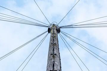 Wooden utility pole with multiple power lines spreading outward against a cloudy sky. Symmetrical perspective view looking up.