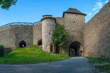 Medieval stone castle with towers and arched windows, surrounded by lush green gardens under a partly cloudy sky. Historic architecture and peaceful atmosphere.