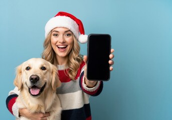 Cheerful woman and her dog celebrating Christmas. Young person in a Santa hat holding a smartphone with a blank screen for a mockup.