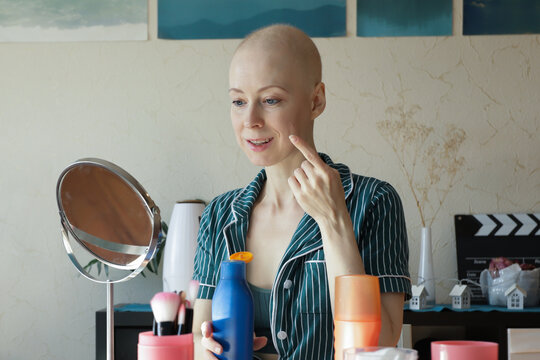 Bald woman after chemotherapy applying SPF skincare at home, showing daily protection routine for sensitive skin of oncology patients. Concept of healthcare, self-care, beauty, and cancer recovery
