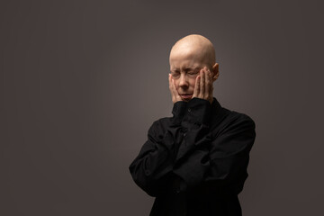 Bald woman after chemotherapy covering her face with hands, concept of sadness, despair, and mental health challenges during illness.