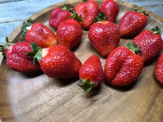 Ripe sweet strawberries in a wooden plate on a wooden
