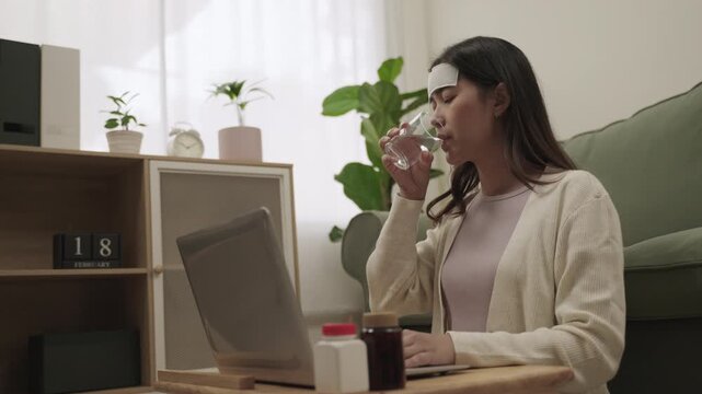 Working from home concept. Young Asian woman employee is symptoms sick and has a headache from the flu use fever cooling gel patch and sitting using laptop computer for working in living room at home.