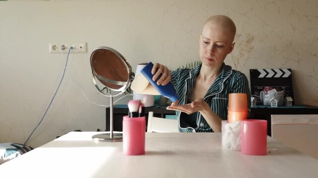 Bald female patient in pajamas applying SPF lotion on her face, symbolizing healthy habits and skin safety after treatment.