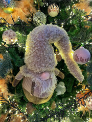 Adorable plush gnome ornament with a long hat, nestled among festive decorations on a Christmas tree, creating a cozy holiday atmosphere and joyful spirit