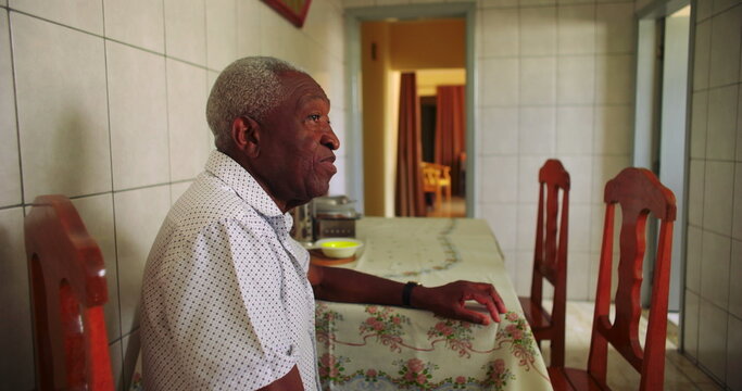 Elderly African American man sitting alone at a dining table in a quiet kitchen, reflecting solitude and introspection in a peaceful home environment