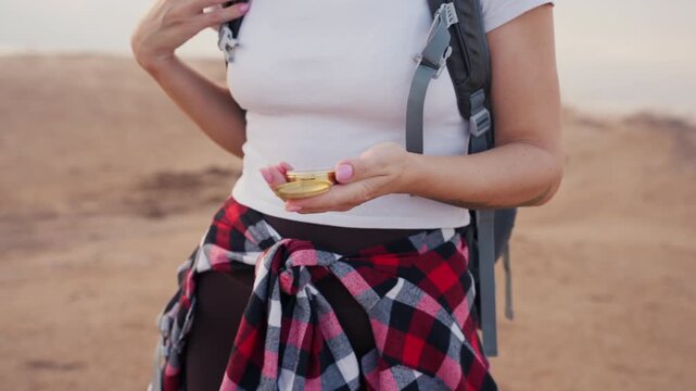 Close-up of woman hiker hold an open golden compass over backpack in desert landscape, navigating journey and embracing adventure, exploration, and nature