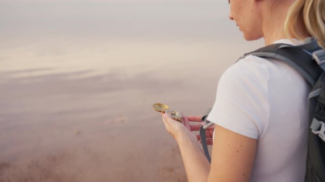 Blonde woman wearing backpack use vintage brass compass to navigate through natural landscape while hiking, ensuring woman stays on correct path for adventure