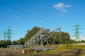 Steel framework of a new power transmission tower under construction beside existing green pylons