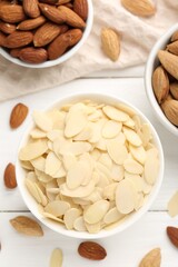 Fresh almond flakes and whole nuts on white wooden table, flat lay