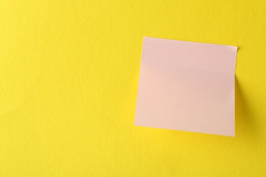 Blank pink note on yellow background, top view. Space for text