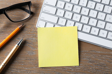 Blank note, glasses, keyboard and pencil on wooden table, flat lay. Space for text