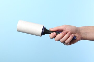 Woman with lint roller on light blue background, closeup