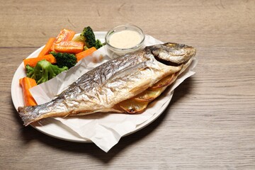Tasty grilled fish, vegetables and sauce on wooden table, closeup. Space for text