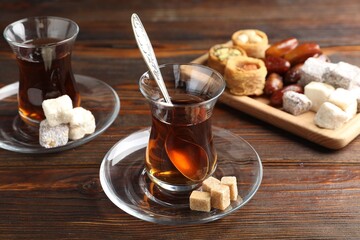 Traditional Turkish tea, brown sugar and sweets on wooden table, closeup