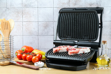 Electric grill with raw meat and vegetables on wooden table