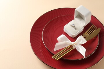 Beautiful table setting for romantic dinner and box with engagement ring on beige background,...