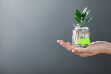 Woman holding jar with blank note, money and sprout on grey background, closeup. Space for text