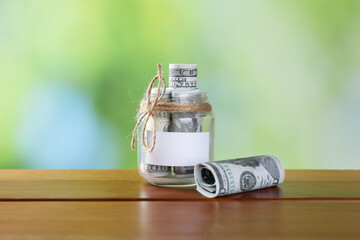 Jar with blank note and money on wooden table against blurred background, closeup