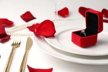 Beautiful table setting for romantic dinner and box with engagement ring on white background,...