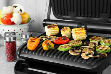 Electric grill with delicious vegetables on light table, closeup
