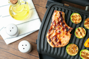 Electric grill with steak and vegetables on wooden table in kitchen, flat lay