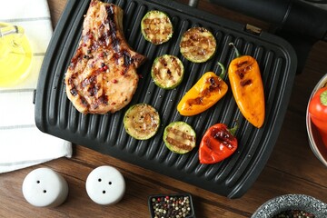 Electric grill with steak and vegetables on wooden table in kitchen, flat lay
