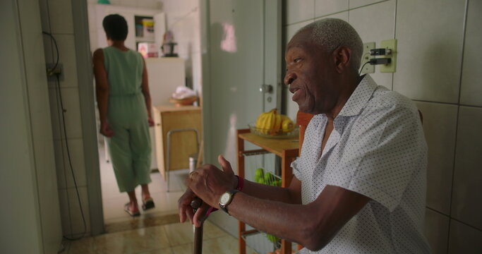 Elderly man sitting pensively in the kitchen, holding a cane, reflecting calmness, dignity, and introspection, capturing a moment of peaceful solitude