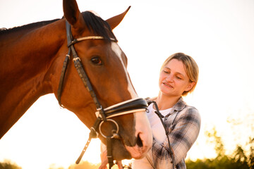 Fototapeta premium Woman takes care of horse, watching it at sunset. Trust between female rider and horse, harmonious relationship between woman and her pet.