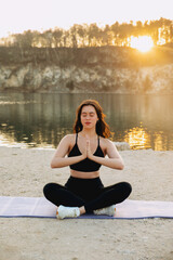 Evening yoga practice by the tranquil lake as the sun sets behind peaceful trees in a serene...