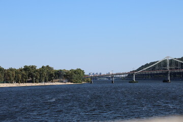 view on Dnipro river, Trukhaniv Island and Parkoviy bridge from quay, Kyiv, 2025