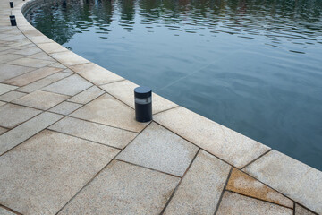 Small cylindrical outdoor light fixture on granite pavement near water surface. Landscape lighting...