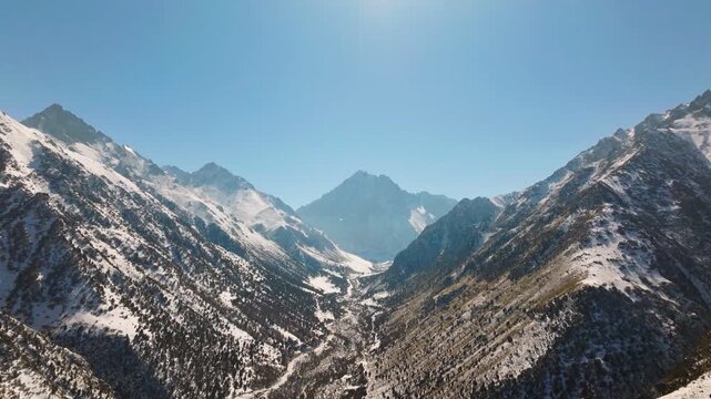 Aerial view captures vast snow-capped mountains in Kyrgyzstan on a sunny winter day. Dolly forward camera movement.