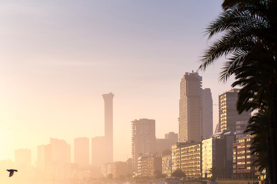 The Benidorm city skyline is silhouetted against the warm, hazy light of a beautiful sunrise. A concept of a peaceful morning in a popular coastal destination.