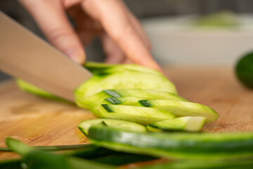 Slicing cucumbers with a large knife on wood cooking board close-up