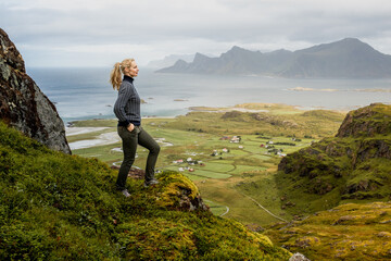 Young beautiful woman posing on top of a hill in Lofoten Norway with incredible views.