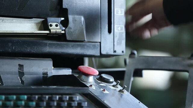 Skilled worker adjusts and maintains complex vintage printing press or typesetting machine. Detailed close-up of hands on intricate industrial components and levers.