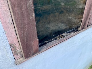 close up of an old wooden window damaged by termites and rainwater, showing decay, rot, and weathered texture as a symbol of aging and poor maintenance.